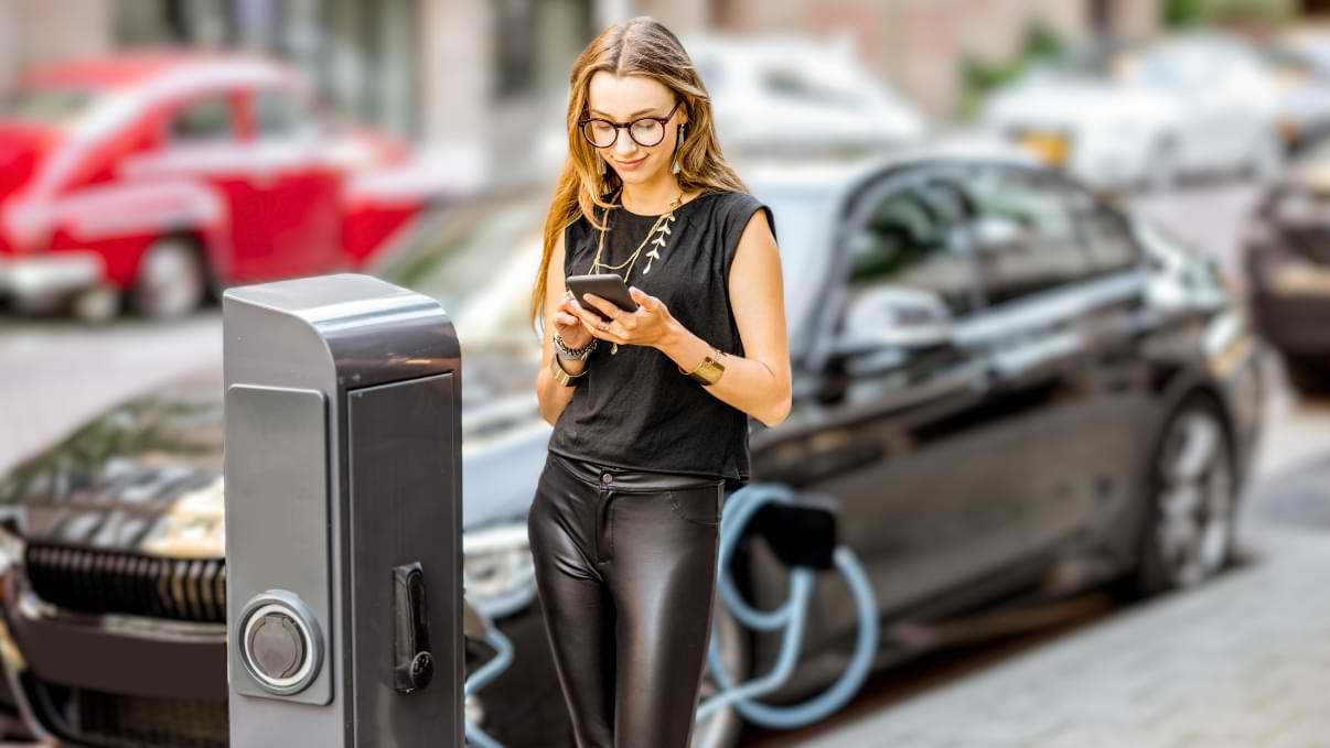 Une femme se tient devant une borne de recharge pour voiture électrique