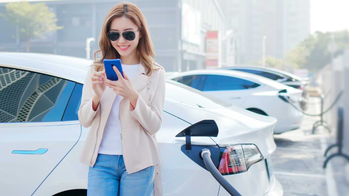 Une femme regarde son smartphone pendant que sa voiture électrique charge