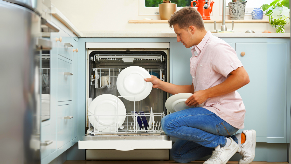 Un homme met une assiette au lave vaisselle